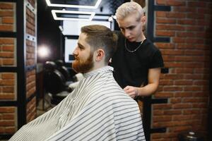 Jeune Beau coiffeur fabrication la Coupe de cheveux de attrayant barbu homme dans salon de coiffure. photo