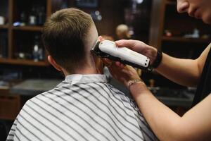 Jeune Beau coiffeur fabrication la Coupe de cheveux de attrayant barbu homme dans salon de coiffure. photo