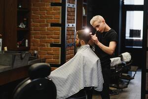 fabrication la Coupe de cheveux Regardez parfait. Jeune barbu homme avoir la Coupe de cheveux par coiffeur tandis que séance dans chaise à salon de coiffure. photo