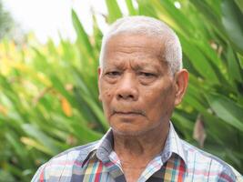 portrait de un personnes âgées asiatique homme souriant et à la recherche à le caméra tandis que permanent dans une jardin. concept de vieilli gens et soins de santé photo