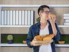 Jeune homme souriant et en portant une panier de pain tandis que permanent dans le bureau. Frais boulangerie produit. nourriture concept photo
