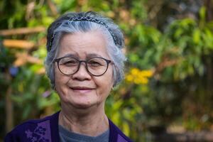 portrait de une Sénior femme avec court gris cheveux portant lunettes, souriant, et à la recherche à le caméra tandis que permanent en plein air. espace pour texte. concept de vieilli gens et soins de santé photo