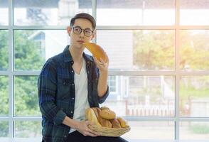 Jeune homme en portant une panier de pain et à la recherche une façon tandis que séance sur le table dans le bureau. Frais boulangerie produit. espace pour texte. nourriture concept photo