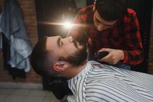 Jeune barbu homme avoir barbe la Coupe de cheveux par coiffeur. salon de coiffure thème. photo