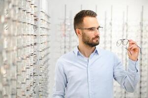 Jeune homme choisir lunettes à optique magasin photo