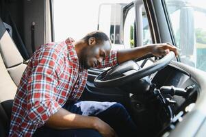fatigué de travail. séance dans le cabine. Jeune africain américain un camion chauffeur est avec le sien véhicule à jour. photo
