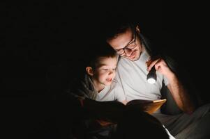 père et le sien peu fils en train de lire heure du coucher récit à maison. photo