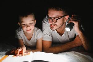 père et le sien peu fils en train de lire heure du coucher récit à maison. photo