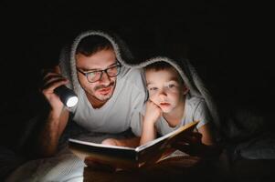 père et le sien peu fils en train de lire heure du coucher récit à maison. photo