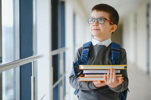 écolier avec cartable et livres dans le école. éducation concept. retour à école. écolier Aller à classe. élégant garçon avec sac à dos. garçon prêt à étude photo