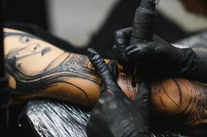 tondu proche en haut de une barbu tatouage artiste travail à le sien studio tatouage manche sur le bras de le sien Masculin client. homme avoir tatoué par professionnel tatoueur photo