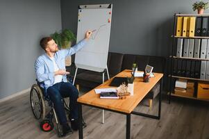 une homme dans une fauteuil roulant est travail dans une bureau. le concept de travail de gens avec handicapées. photo