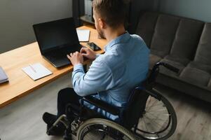 désactivée la personne dans le fauteuil roulant travaux dans le Bureau à le ordinateur. il est souriant et passionné à propos le flux de travail photo