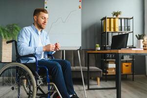 une homme dans une fauteuil roulant est travail dans une bureau. le concept de travail de gens avec handicapées. photo