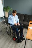 désactivée homme d'affaire séance dans fauteuil roulant en utilisant ordinateur à lieu de travail photo