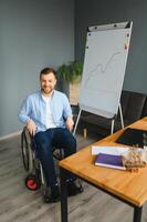 une homme dans une fauteuil roulant est travail dans une bureau. le concept de travail de gens avec handicapées. photo