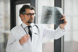 plus âgée homme médecin examine radiographie image de poumons dans une clinique photo