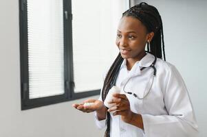 proche en haut tondu horizontal coup de souriant africain femelle médecin ou pharmacien, en portant coloré cloques avec pilules, montrant leur à caméra, tandis que permanent dans pharmacie ou hôpital. photo