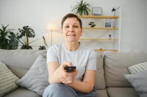 portrait de content plus âgée femme en changeant canal sur télévision. photo