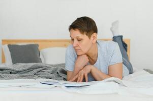 plaisir et Accueil concept - souriant âge moyen femme en train de lire livre et mensonge sur canapé à maison. photo