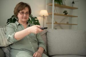 personnes, télévision et divertissement concept - Sénior femme dans lunettes avec éloigné contrôle en train de regarder la télé à Accueil photo