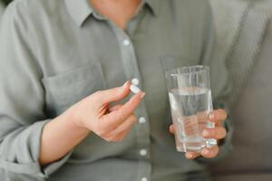 mature Sénior milieu vieilli femme en portant pilule et verre de l'eau prise anti douleur à soulager douleur, médicament suppléments vitamines, antibiotique médicament, Médicaments pour vieux la personne concept, proche en haut voir. photo