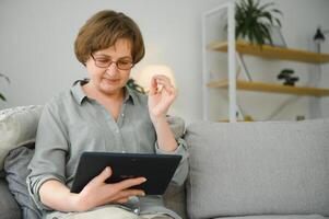 Sénior femme à la recherche et en riant à sa numérique tablette sur canapé photo