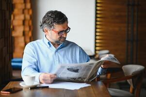 actif Sénior homme en train de lire journal et en buvant café dans restaurant photo