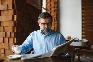 actif Sénior homme en train de lire journal et en buvant café dans restaurant photo