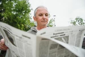 portrait de Sénior homme en train de lire sur banc pendant été journée. photo