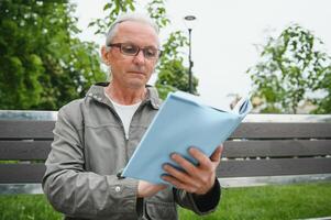 Sénior homme en train de lire une livre dans le parc. photo