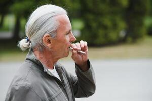 un vieux Sénior homme fumeur cigarette dehors, fumée dépendance, mal habbit photo