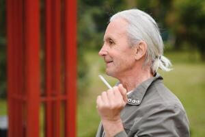 un vieux Sénior homme fumeur cigarette dehors, fumée dépendance, mal habbit photo