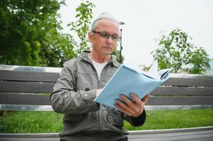 portrait de Sénior homme en train de lire sur banc pendant été journée. photo