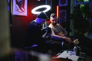 tatouage artiste démontre le processus de avoir noir tatouage avec peindre. Maître travaux dans noir stérile gants photo