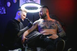 tatouage artiste démontre le processus de avoir noir tatouage avec peindre. Maître travaux dans noir stérile gants photo