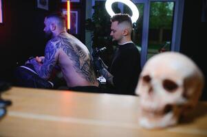 tatouage. homme création une image sur le sien retour par une professionnel tatouage artiste photo