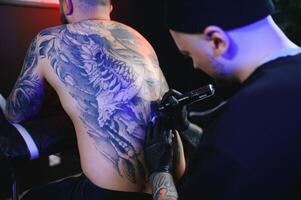 tatouage. homme création une image sur le sien retour par une professionnel tatouage artiste photo