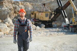 une ouvrier dans une casque des stands sur le Contexte de un excavatrice dans une carrière photo