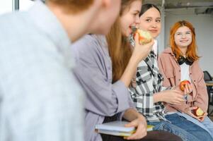 de bonne humeur élèves sont séance à bureaux et en mangeant un Pomme pendant une Pause photo