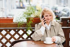 mode portrait de Jeune femme implantation à le table avec tasse de café, thé dans rue café. photo