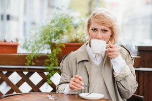 mode portrait de Jeune femme implantation à le table avec tasse de café, thé dans rue café. photo