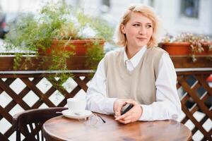 mode portrait de Jeune femme implantation à le table avec tasse de café, thé dans rue café. photo