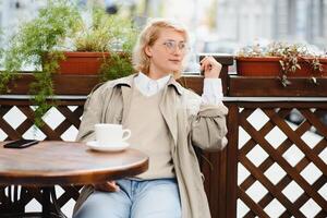 mode portrait de Jeune femme implantation à le table avec tasse de café, thé dans rue café. photo