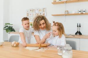 famille apprentissage Nouveau recette ensemble. content maman et des gamins mélange Ingrédients pour fait maison gâteau, tarte ou biscuit pâte dans le cuisine. photo