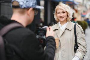 une fille fait du une Blog avec une cameraman sur le rue. Jeune femme blogueur, journaliste tournage avec une professionnel caméra et vidéaste. photo