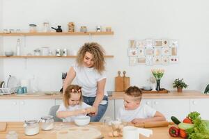 content famille dans le cuisine. mère et les enfants en train de préparer le pâte, cuire biscuits photo