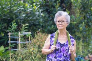 un personnes âgées asiatique femme avec court gris coiffure décontractée Vêtements souriant et exercice tandis que permanent dans une jardin. espace pour texte. concept de vieilli gens et soins de santé photo