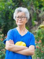 un personnes âgées femme avec court gris cheveux bras franchi, souriant et à la recherche à le caméra tandis que permanent en plein air. concept de vieilli gens et soins de santé photo