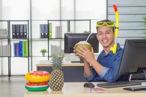 Jeune homme portant une plongée masque jaune, souriant et en portant une Frais noix de coco dans le sien bureau. il rêves de le mer car le vacances à venir bientôt. vacances concept photo